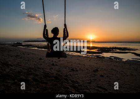 Die Silhouette eines jungen Frau auf einer Schaukel in einem Strand von Gili Air, Gili Inseln, Indonesien. Stockfoto
