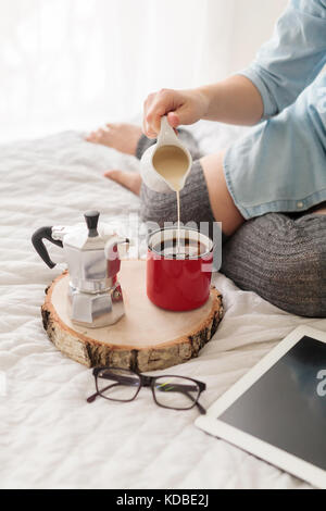 Frau gießen Milch in die roten Becher Kaffee Stockfoto