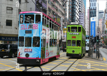 An der Unterseite der Gebäude, bunte doppelstöckigen Straßenbahn vom Hong Kong Straßenbahnen mit großen Werbung auf seinen Seiten. Riesige Konica Minolta Anzeige *** Stockfoto