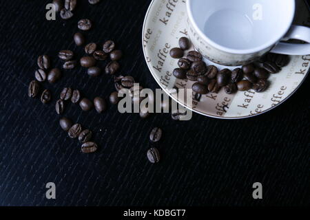 Moccatasse Kaffeetasse mit verstreuten Kaffee Bohnen in schwarzem Tisch-Mocca Tasse Kaffee Tasse mit verstreuten Kaffeebohnen auf schwarz Tabelle Stockfoto