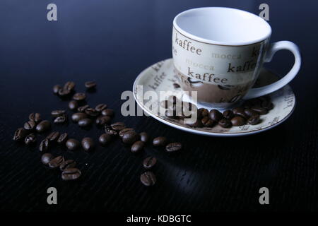 Moccatasse Kaffeetasse mit verstreuten Kaffee Bohnen in schwarzem Tisch-Mocca Tasse Kaffee Tasse mit verstreuten Kaffeebohnen auf schwarz Tabelle Stockfoto