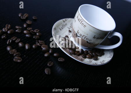 Moccatasse Kaffeetasse mit verstreuten Kaffee Bohnen in schwarzem Tisch-Mocca Tasse Kaffee Tasse mit verstreuten Kaffeebohnen auf schwarz Tabelle Stockfoto