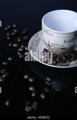 Moccatasse Kaffeetasse mit verstreuten Kaffee Bohnen in schwarzem Tisch-Mocca Tasse Kaffee Tasse mit verstreuten Kaffeebohnen auf schwarz Tabelle Stockfoto