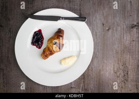 Croissant auf einem weißen Teller mit Black Cherry bewahren und Butter Stockfoto
