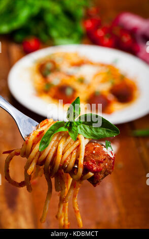 Gabel Spaghetti mit Basilikum und frikadelle mit Platte in der Ferne. Stockfoto
