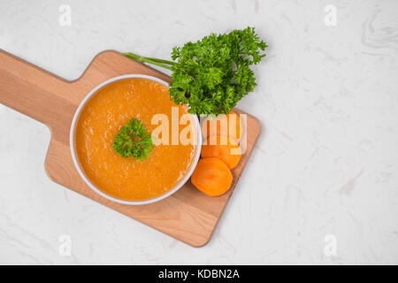 Karottensuppe mit Sahne und Petersilie auf weißem Stein. Ansicht von oben. Textfreiraum Stockfoto