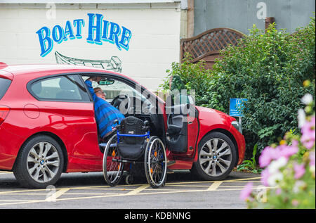 Behinderte Menschen klettern in ein Auto vom Rollstuhl aus. Stockfoto