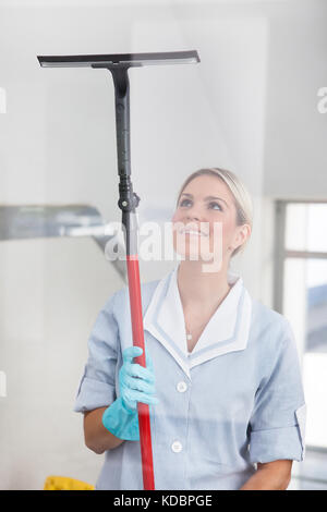 Glückliche Frau reinigen Glas mit Gummi Glasreiniger Stockfoto