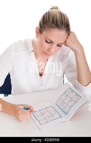 Junge Frau auf weißem Hintergrund Sudoku lösen Stockfoto