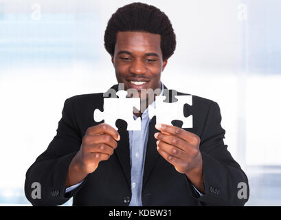 Porträt eines glücklichen jungen Geschäftsmann mit Jigsaw Puzzle Stockfoto