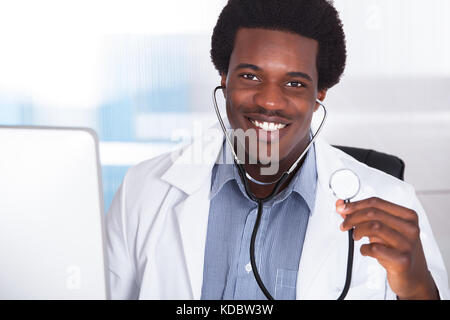 Porträt von glücklich Arzt mit Stethoskop am Schreibtisch sitzt Stockfoto