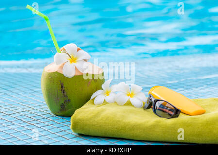 Grün, einem Handtuch und einem Zubehör in der Nähe eine saftige Kokosnuss mit Blumen am Rand des Pools eingerichtet Stockfoto