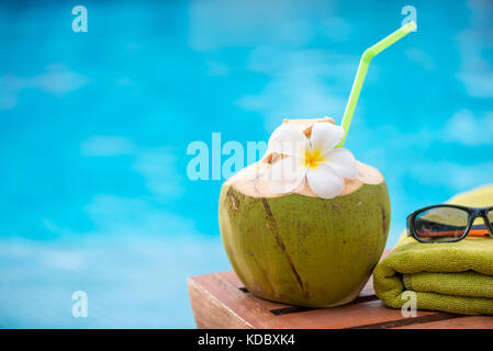 Kokosnuss mit einem Strohhalm am Rande eines Liegestuhl vor blauem Wasser pool Hintergrund Stockfoto