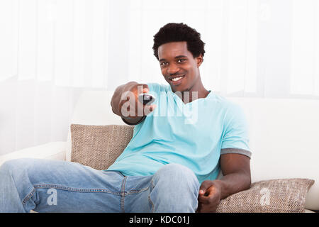 Happy afrikanischen Jungen Mann Fernsehen zu Hause beobachten Stockfoto