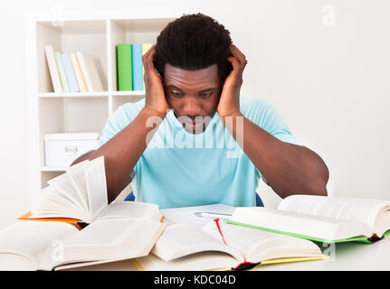 Junge afrikanische Mann zu Hause studieren mit eine Menge Bücher besorgt Stockfoto