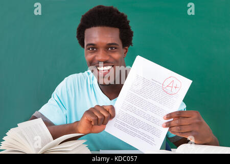 Glücklich afrikanische männlichen Studenten zeigt eine Papier mit perfekten Grade ein Plus im Klassenzimmer Stockfoto