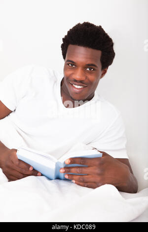 Junge afrikanische glücklich Lektüre seines Buches auf Bett Stockfoto
