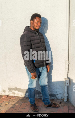 Porträt eines nigerianischen Mannes mit schwarzer Jacke an der weißen Wand, Italien. Stockfoto