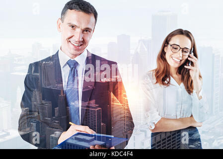 Lächelnder Mann mit einem Ordner, während seine Kollegen sprechen über das Telefon Stockfoto