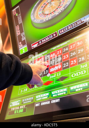 Mann mit gekreuzten Fingern mit Wetten zu festen Quoten Klemmen (FOBT terminal Wetten zu festen Quoten) in Buchmacher. England. Großbritannien Stockfoto