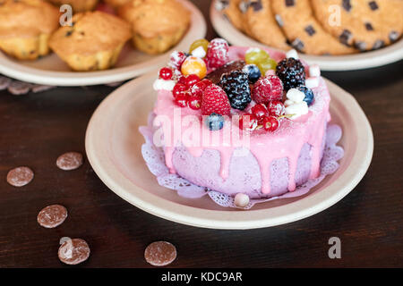 Süße Käsekuchen mit frischen Beeren und Joghurt Creme. Lecker Himbeeren Kuchen mit frischen Erdbeeren, Himbeeren, Heidelbeeren, Johannisbeeren und Blackberry Früchte auf rustikalen Holzmöbeln Hintergrund. Stockfoto