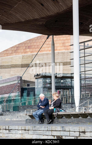 Ein Paar sitzt zusammen an einem nassen Frühlingstag in Cardiff Bay, Cardoff. WA;es. UK Stockfoto