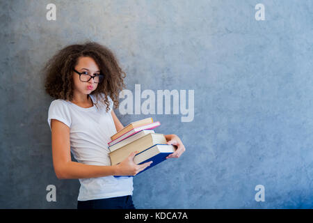 Portrait von jugendlichen Mädchen mit Brille steht neben der Wand und hält mehrere Bücher Stockfoto