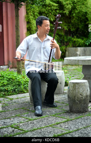 Alte chinesische Mann spielt erchu oder chinesische Geige im Garten am Abend Stockfoto