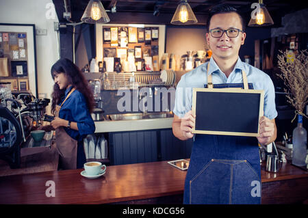 Portrait von lächelnden asiatischer barista Holding leere Schiefertafel Menü im Coffee Shop. Cafe Restaurant Service, Inhaber kleiner Unternehmen, die Lebensmittel- und Getränkeindustrie Stockfoto