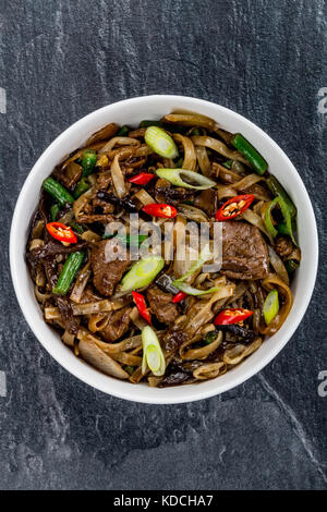 Im chinesischen Stil wok gebratenes Rindfleisch mit Pilzen und Nudeln auf einem schwarzen Schiefer Küche Fliesen rühren Stockfoto