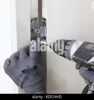 Ein Arbeiter installiert im Rahmen der Sanierung eines Wohnblocks in London, Großbritannien, eine verborgene näher an einer neuen Brandschutztür. Stockfoto