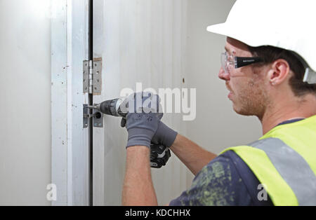 Ein Arbeiter installiert im Rahmen der Sanierung eines Wohnblocks in London, Großbritannien, eine verborgene näher an einer neuen Brandschutztür. Stockfoto