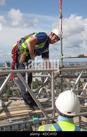 Zwei Gerüstbauer Montieren einer Plattform auf einem Turm hoch über London. Zeigt die richtige Sicherheitsausrüstung einschließlich Kabelbäume. Stockfoto