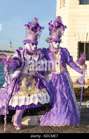 2017 Karneval in Venedig, Venedig, Italien, zwei Frauen in klassischen lila Kostüme bei Sonnenuntergang vor der San Giorgio Maggiore Leuchtturm posiert mit der Stockfoto