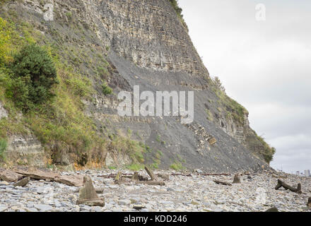 Gefallenen Felsen und gebrochene Stahlbeton Klumpen am Strand, und Gesteinsschichten in Klippen in der Nähe von Llanberis Kopf, Penarth, Wales, Großbritannien Stockfoto