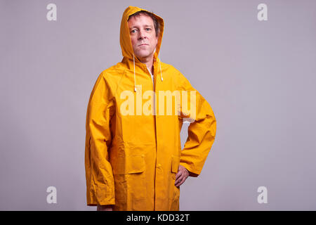 Eine ernste Mann mittleren Alters stehend in einem gelben Regenmantel Stockfoto