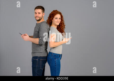 Ein schönes junges Paar Rücken an Rücken stehend, während halten und mit ihren smartphones Stockfoto