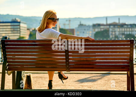 Eine schöne, junge blonde Frauen sitzen auf einer Bank in den Sonnenuntergang auf der Riverside Stockfoto