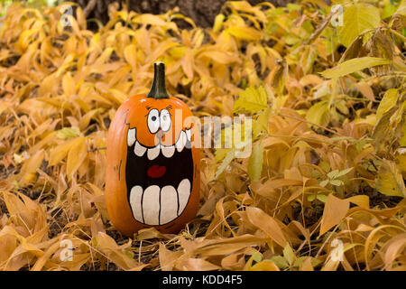 Nahaufnahme der ein handgemaltes lachend Jack o'Lantern unter getrocknete Blätter mit einem Baum im Hintergrund. geringe Tiefenschärfe. Stockfoto