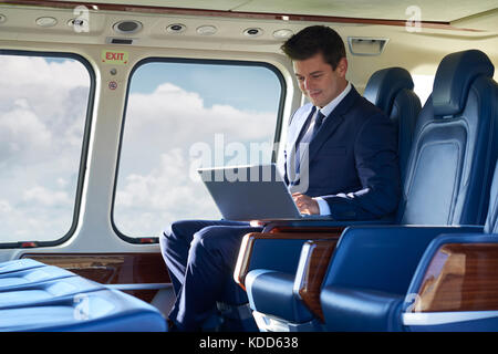 Unternehmer Arbeiten am Laptop im Hubschrauber der Kabine während des Fluges Stockfoto