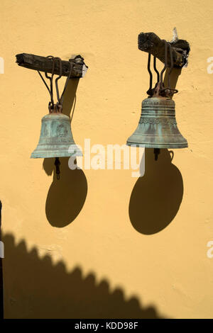 Glocken hängen an der Wand der Kirche, Sonne und Schatten in Longos, Paxos, Griechenland Stockfoto