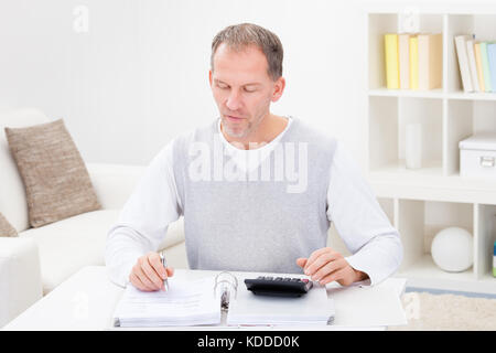 Reifer Mann sitzen auf der Couch zu Hause Holding Taschenrechner und Rechnungen Stockfoto