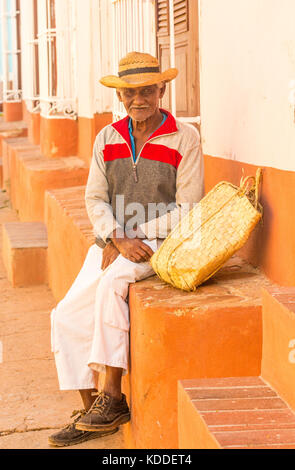 Lächelnd lokale kubanischen Mann mit Hut außerhalb eines Hauses sitzend beobachten, den Tag durch in der Nähe der Plaza Major, Trinidad, Kuba, Karibik Stockfoto