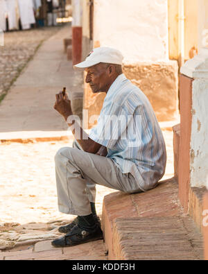 Lächelnd lokale kubanischen Mann mit Hut außerhalb eines Hauses sitzend beobachten, den Tag durch in der Nähe der Plaza Major, Trinidad, Kuba, Karibik Stockfoto