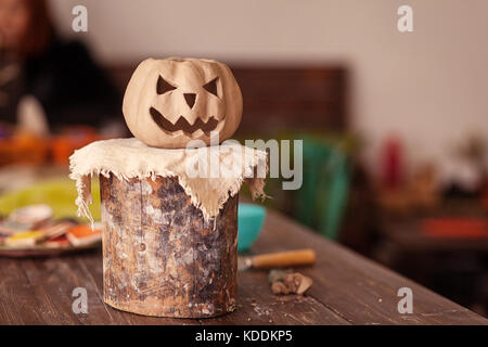 Eine kleine Ton Kürbis mit Jack's Gesicht für Halloween steht auf einem Stand aus Holz auf einem hölzernen Tisch in einem schönen Workshop Stockfoto