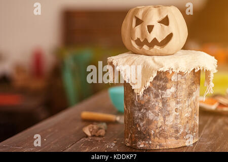 Eine kleine Ton Kürbis mit Jack's Gesicht für Halloween steht auf einem Stand aus Holz auf einem hölzernen Tisch in einem schönen Workshop Stockfoto