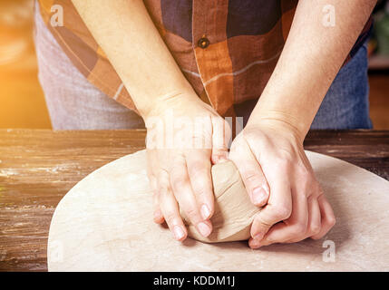 Eine junge Frau in einem Plaid Shirt und Jeans knetet den Ton mit den Händen vor Arbeiten an der Töpferei Kreis eine Platte, die auf einer hölzernen Kreis in der Arbeit Stockfoto