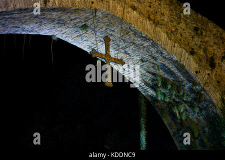 Hängende Kreuz unter der alten römischen Brücke (Puente Romano), 13.jahrhundert, über den Fluss Sella in der Nacht in Cangas de Onis. Asturien. Spanien. Stockfoto