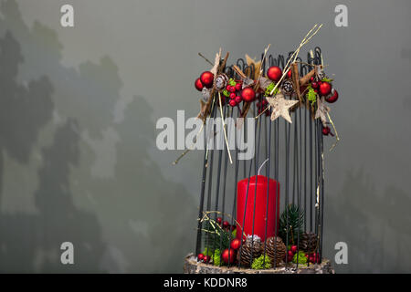 Weihnachten rote Kerze auf einem Baumstumpf mit Metall Stäbchen und Zapfen Tanne auf grauem Hintergrund Stockfoto