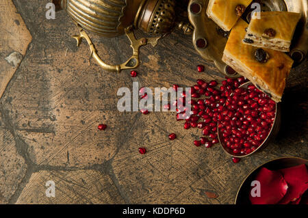 Körner und Samen der Granatapfel mit einem Kupfer Kanne auf eine alte dekorative Stein. Eine antike Kupfer Kanne mit einem Granatapfel und Kuchen auf einem alten Fliesen Stockfoto